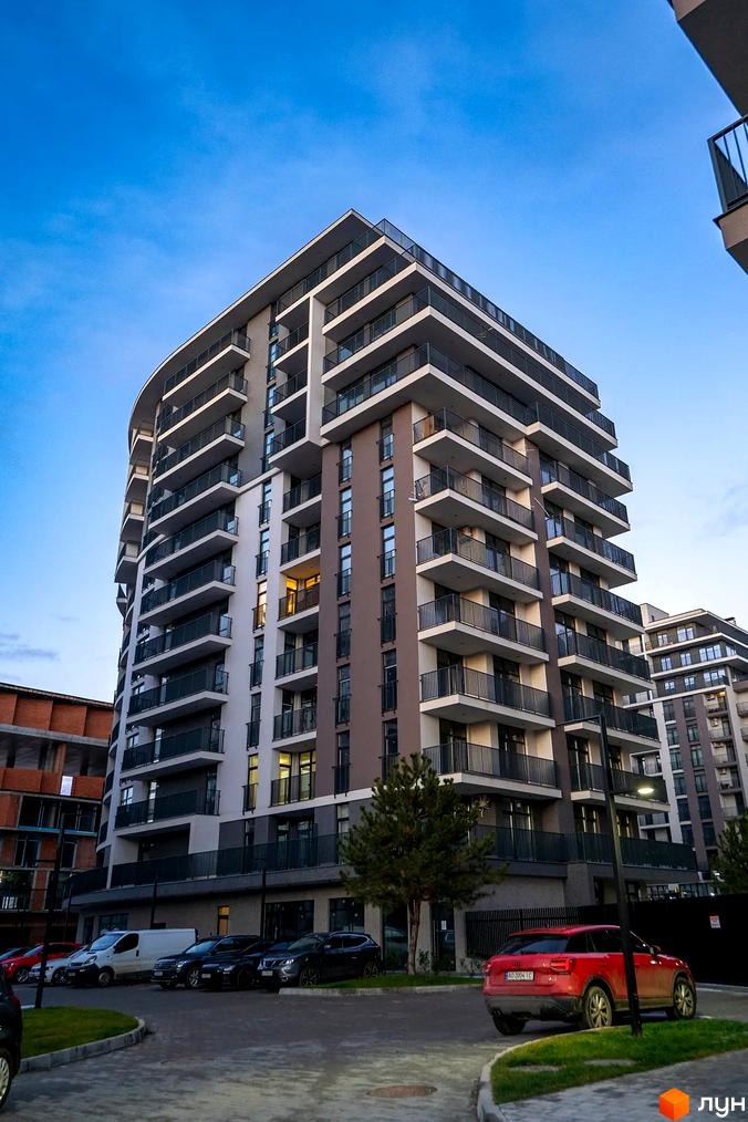 Зовнішній вигляд новобудови ЖК Crystal з балконами та паркуванням автомобілів біля будинку. Комплекс має багатоповерхову забудову та прибудинкову територію.