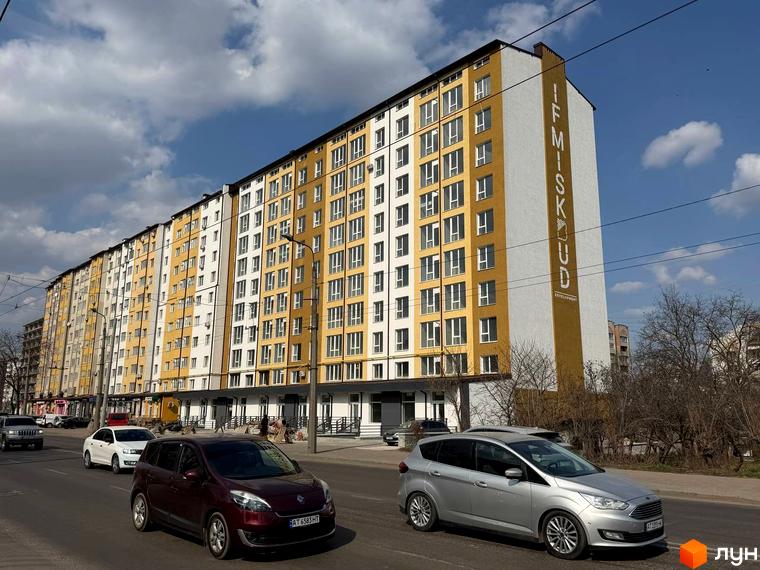 Новобудова IF MISKUD на вул. Галицька, 92, з жовто-білим фасадом та вікнами, на фоні неба з хмарами. Перед будинком проїжджають автомобілі.