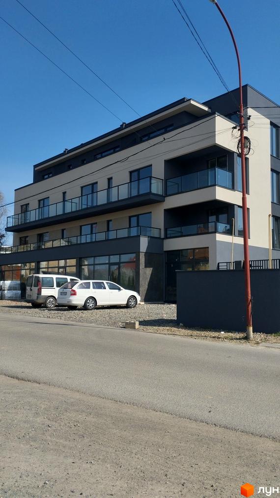 Сучасна новобудова на вул. Срібляста з балконами та великими вікнами, поруч припарковані автомобілі та дорога.