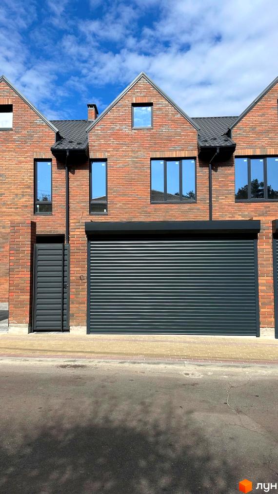 Фасад будинку з цегляним оздобленням, великими вікнами та ролетами. Поруч розташована прибудинкова територія з бруківкою.