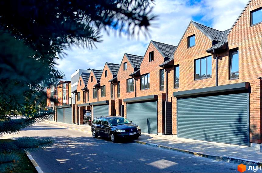 Новобудова на вул. Стуса, 59: цегляні будинки з гаражними воротами та вікнами, асфальтована дорога та зелені насадження.