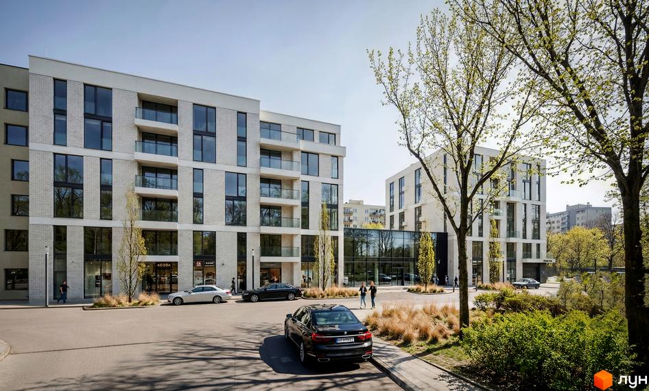 Білі багатоквартирні будинки з великими вікнами та скляними балконами на вул. Замарстинівська, 83б. На першому поверсі є магазини, поруч дерева.