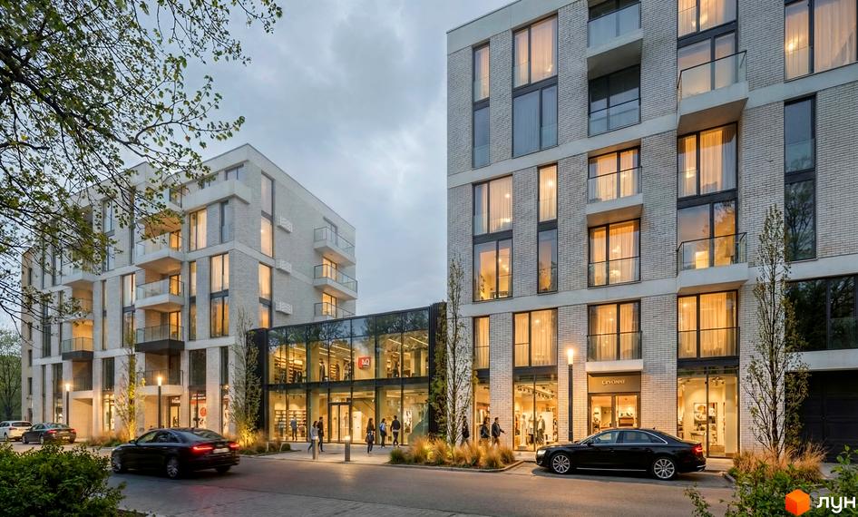 Зображення житлового комплексу на вул. Замарстинівська, 83б з фасадами зі світлої цегли, великими вікнами та балконами. На передньому плані дорога, автомобілі та зелені насадження.