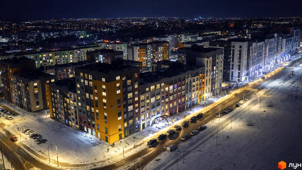 Житловий комплекс На Щасливому: будинки з різнокольоровими фасадами, освітлені вікна, засніжена територія з дорогами та парковками.