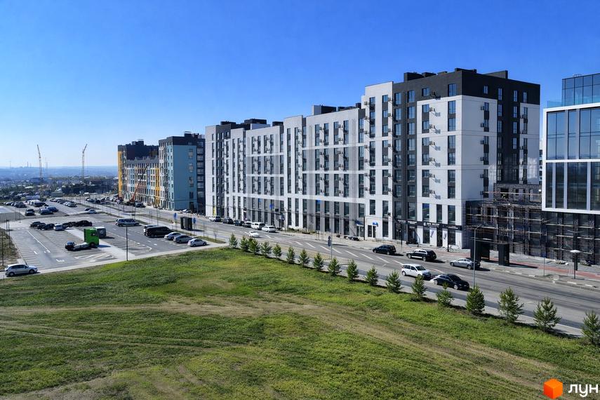 Житловий комплекс На Щасливому: багатоповерхові будинки з біло-сірими та чорними фасадами, поруч дорога, парковка та зелений газон.