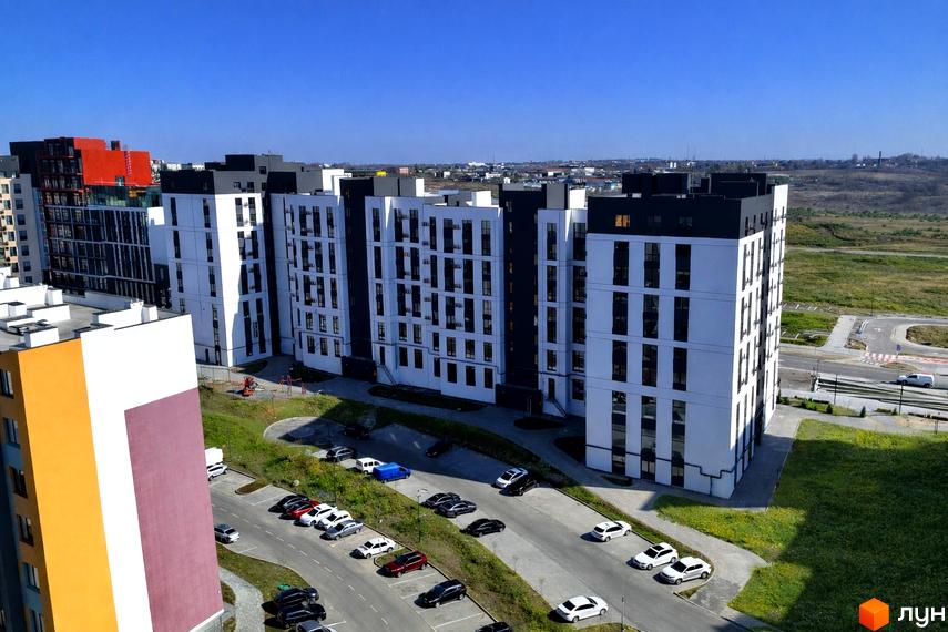 Житловий комплекс На Щасливому має багатоповерхові будинки білого кольору з темними акцентами. Навколо розташовані парковки, зелені зони та дитячий майданчик.