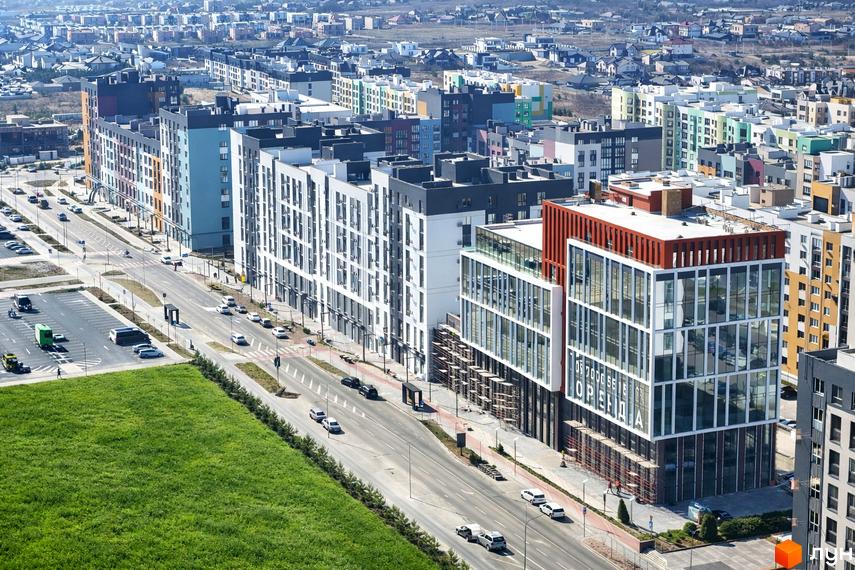 Житловий комплекс На Щасливому: висотні будинки з різнокольоровими фасадами та великими скляними вікнами. Навколо дорога, паркінг та доглянуті зелені газони.