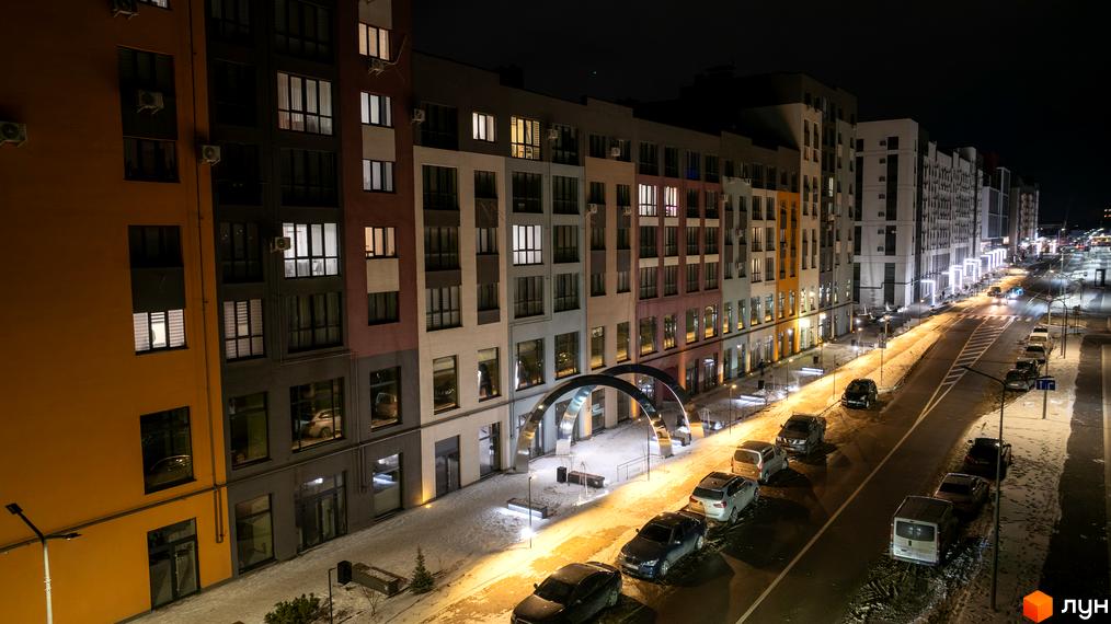 Житловий комплекс На Щасливому вночі, фасади будинків з підсвіткою, прибудинкова територія з паркуванням автомобілів та засніженою дорогою.