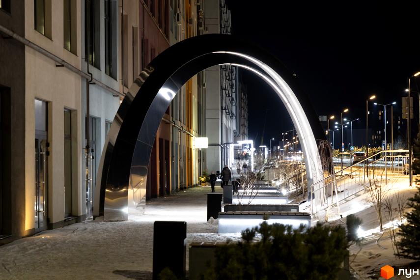 Житловий комплекс На Щасливому: архітектурний простір з підсвіченою аркою та лавами, зимовий вечір.