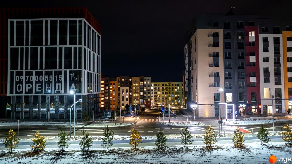 Житловий комплекс На Щасливому вночі з підсвіченими вікнами та фасадами, засніжена прибудинкова територія з ялинками.