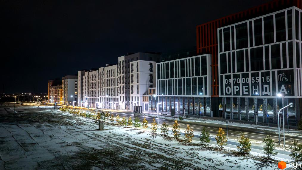 Житловий комплекс На Щасливому вночі, з підсвіченими фасадами та орендованими квартирами, на тлі засніженої території та молодих дерев.