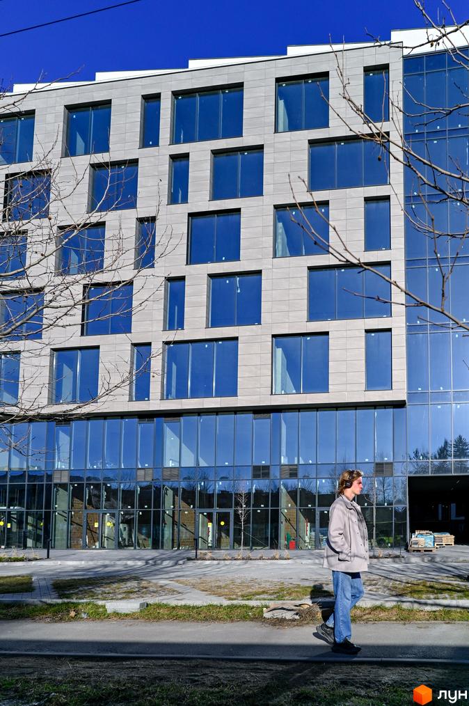 Житловий комплекс Mill Town із сірою фасадною плиткою та великими синіми вікнами. Поруч розташована прибудинкова територія з деревами та тротуаром.