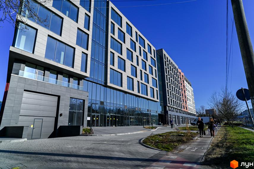 Новобудова ЖК Mill Town з панорамним склінням та сірими фасадами. Поруч облаштований тротуар та зелена зона.