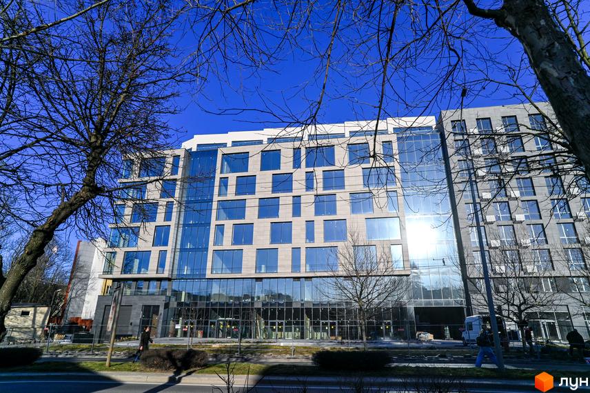 Новобудова Mill Town з панорамним склінням та сірою облицовкою фасаду. Навколо будівлі розташовані дерева та огороджена територія.