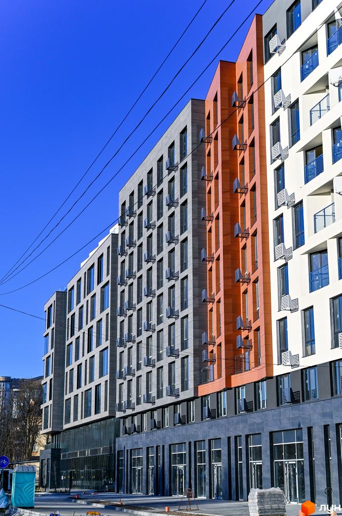 Зовнішній вигляд новобудови ЖК Mill Town з фасадами сірого, помаранчевого та білого кольорів. Поруч видно елементи прибудинкової території.