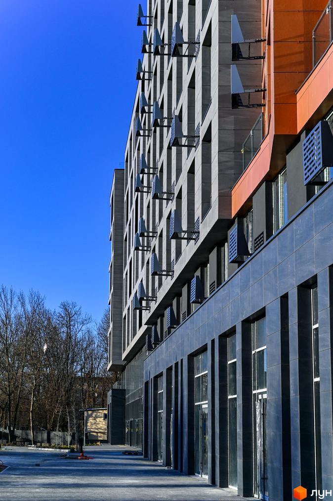 Будівельний проєкт Mill Town з сірим фасадом та оранжевими елементами. Поруч дерева та вхідна група з великими вікнами.