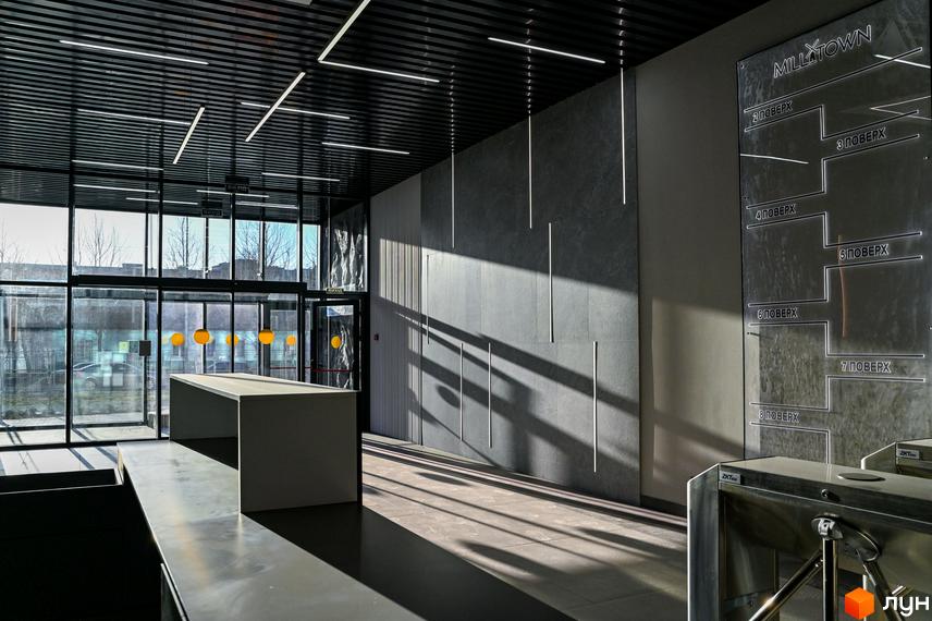 Вхідна група житлового комплексу Mill Town з сірими стінами та підлогою, освітлена сонячним світлом. На стіні розташована навігація по поверхах.