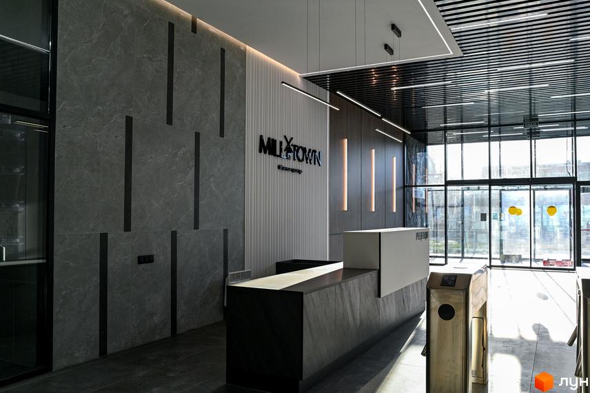 Рецепція житлового комплексу Mill Town з логотипом проєкту та скляним фасадом. Вхідна група з турнікетами та природним освітленням.