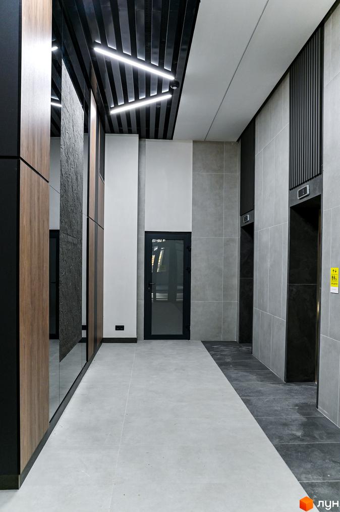 Сучасний хол у ЖК Mill Town з дерев'яними панелями, сірою плиткою та освітленням. Елегантний дизайн інтер'єру новобудови.