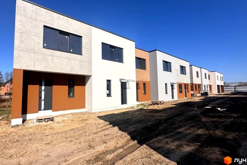 Котеджне містечко Плескіт: Ряд двоповерхових будинків з фасадами світло-сірого, білого та коричневого кольорів. Прибудинкова територія з ґрунтовим покриттям.