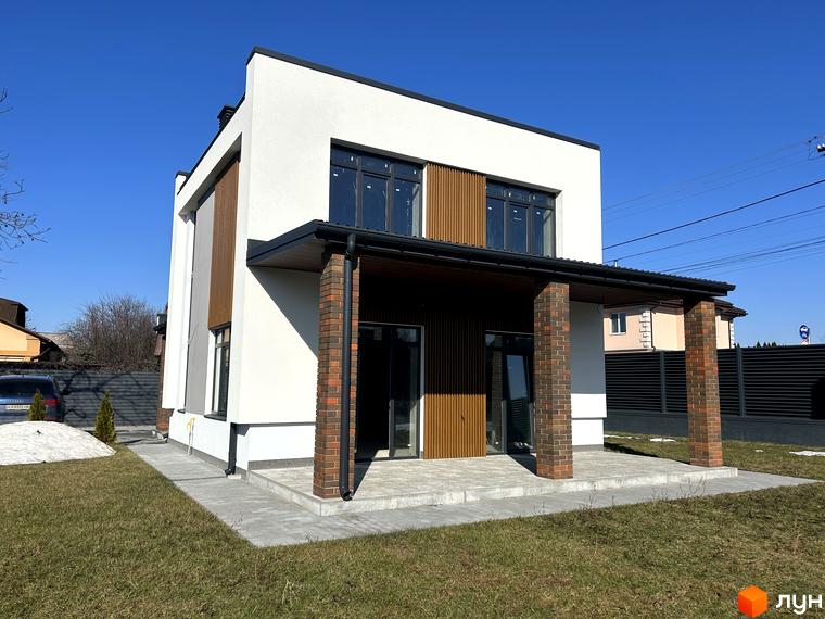 Двоповерховий будинок Котеджного містечка Будинки на Франка з білим фасадом, темними вікнами та цегляними колонами. Навколо будинку зелений газон та вимощена доріжка.