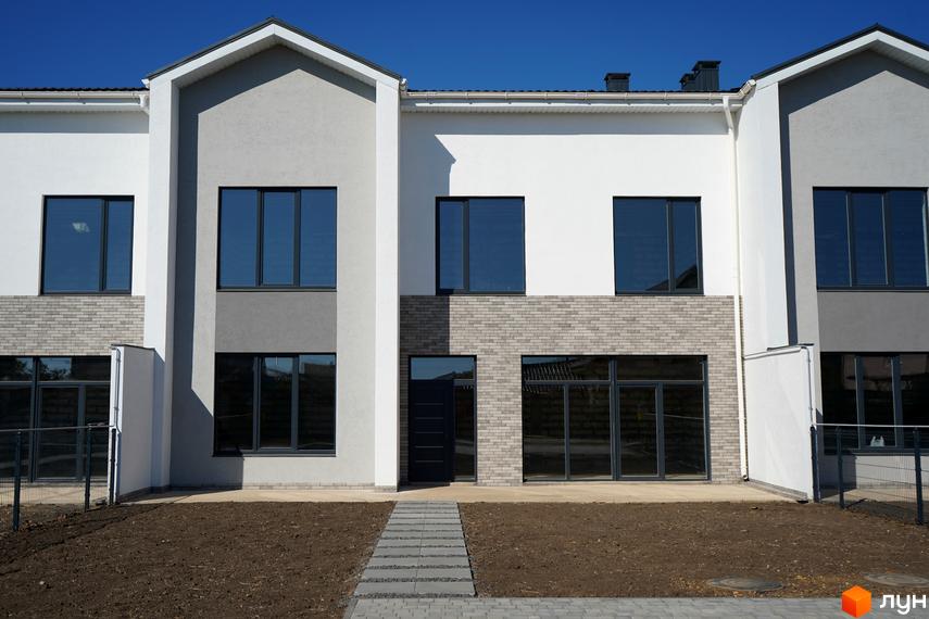 Таунхауси Lazur Village з біло-сірими фасадами та цегляним оздобленням, перед будинками доріжка з плитки та ділянка землі.