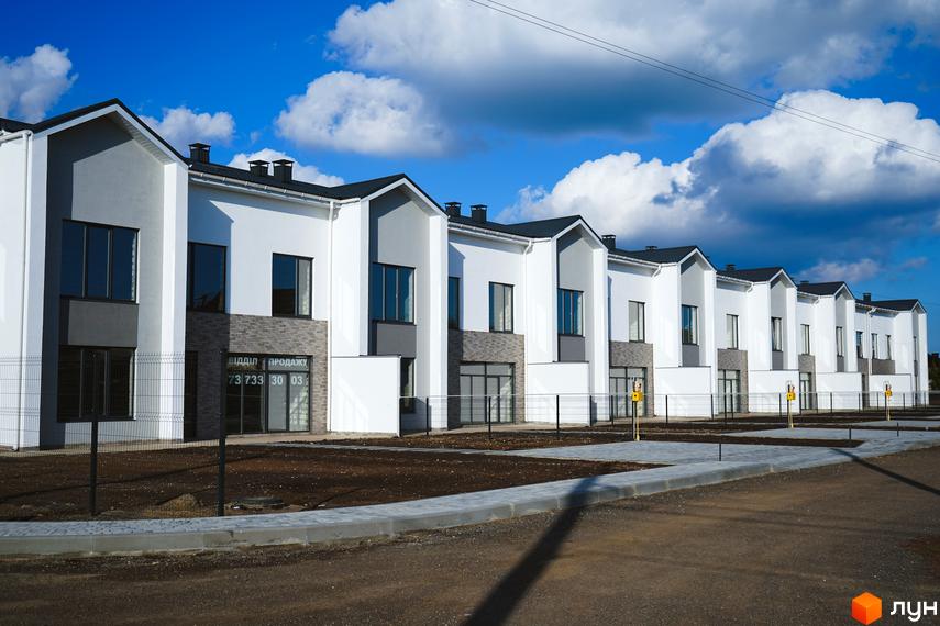 Lazur Village – комплекс таунхаусів з біло-сірими фасадами та темними дахами. Поруч облаштована прибудинкова територія з бруківкою та огорожею.