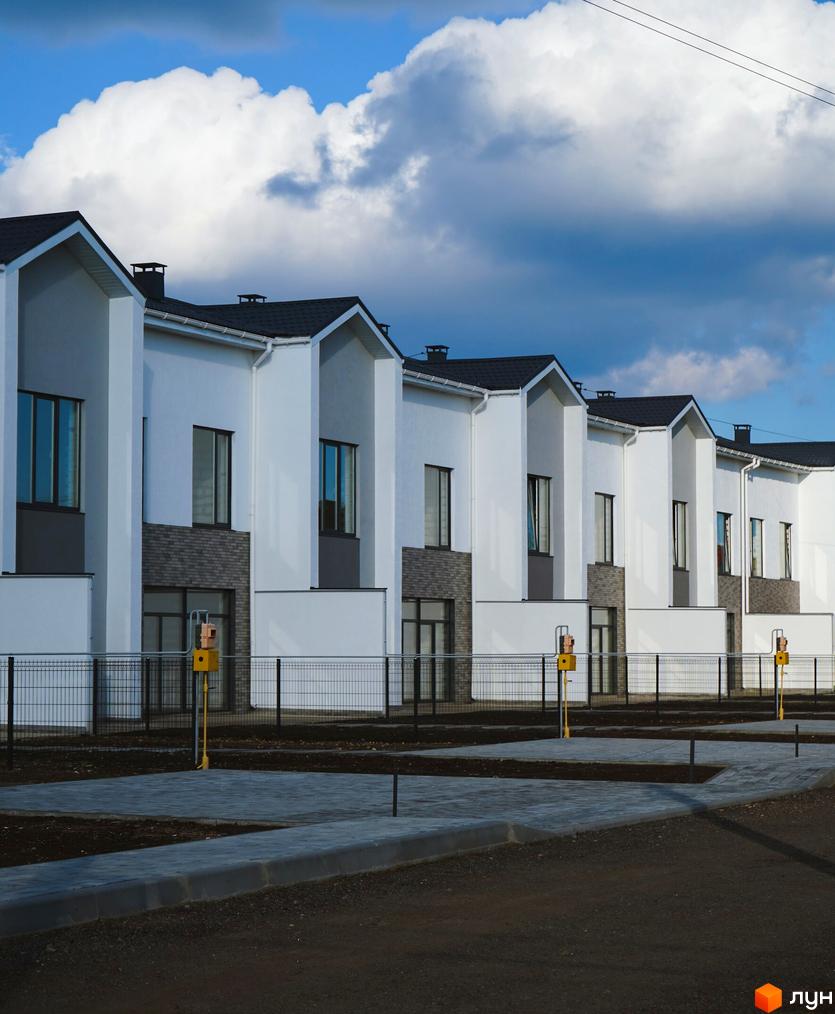 Таунхауси Lazur Village з білими фасадами та темними дахами, огороджена територія з доріжками та газонами.