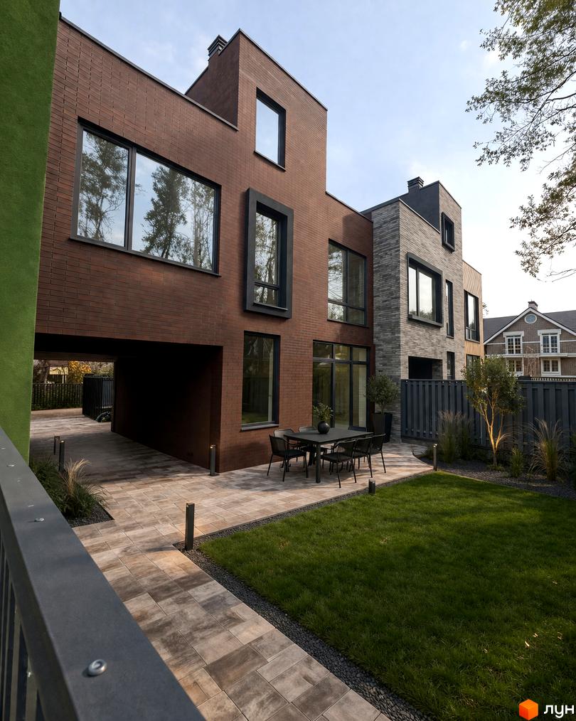 Таунхауси Madera House з цегляним фасадом та великими вікнами, з терасою та зеленою галявиною.