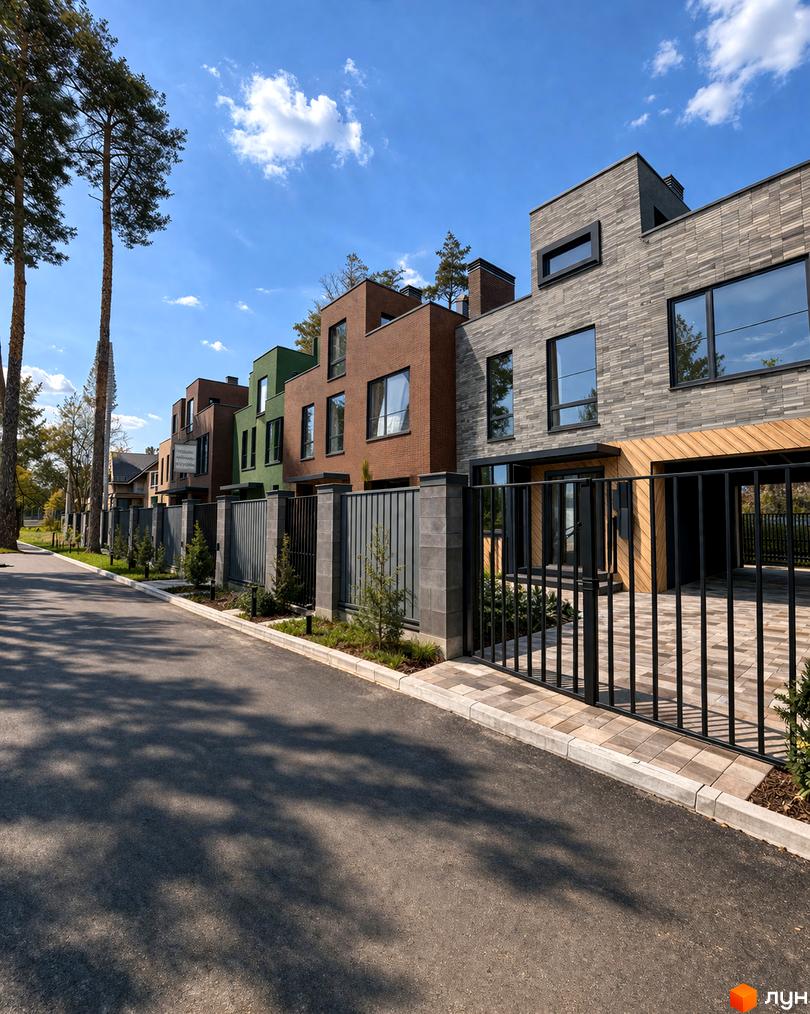 Таунхауси Madera House з цегляним фасадом та зеленими вставками, огороджені парканом. Поруч асфальтована дорога та зелені насадження.