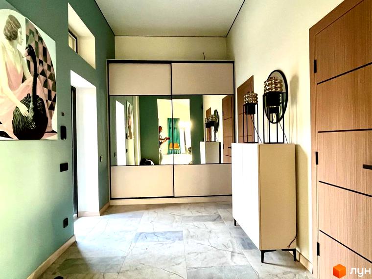 Коридор Котеджного містечка TAO Residence з дзеркальною шафою, картиною на зеленій стіні та дерев'яними дверима.