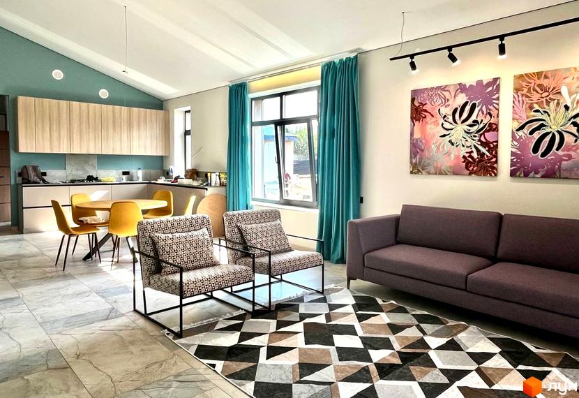 Інтер'єр кухні-вітальні в КМ TAO Residence з обідньою зоною та диваном. Вікна з бірюзовими шторами виходять на подвір'я.