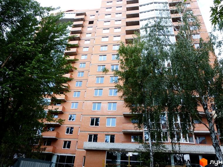 Будівельний проєкт Молодіжний-2: цегляний будинок з балконами та великими вікнами, оточений деревами. Зовнішній вигляд новобудови в місті.
