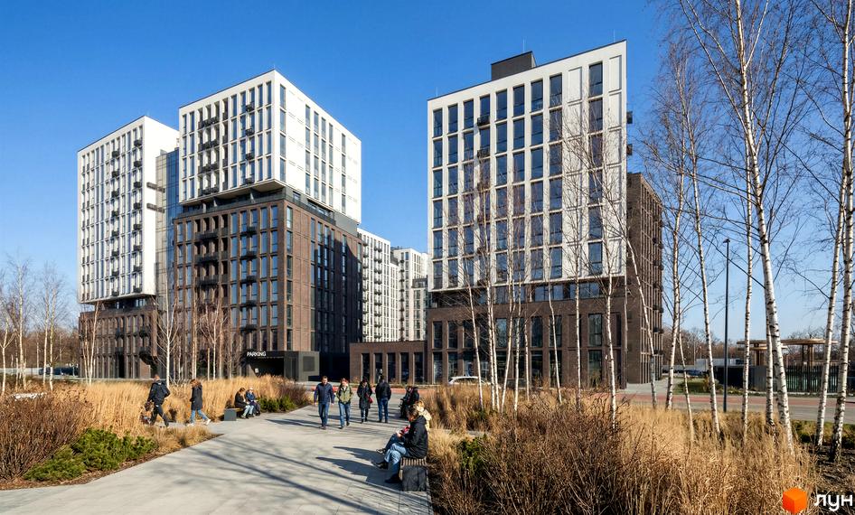 Новобудова Nova City з цегляним та білим фасадами, балконами та панорамними вікнами. Навколо облаштована прибудинкова територія з деревами та зонами відпочинку.