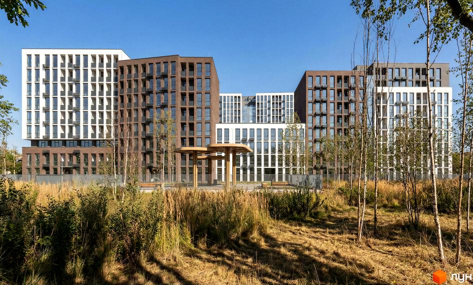 Житловий комплекс Nova City з фасадами з білої та коричневої цегли, вікнами різних розмірів та зеленою прибудинковою територією з деревами та травою.