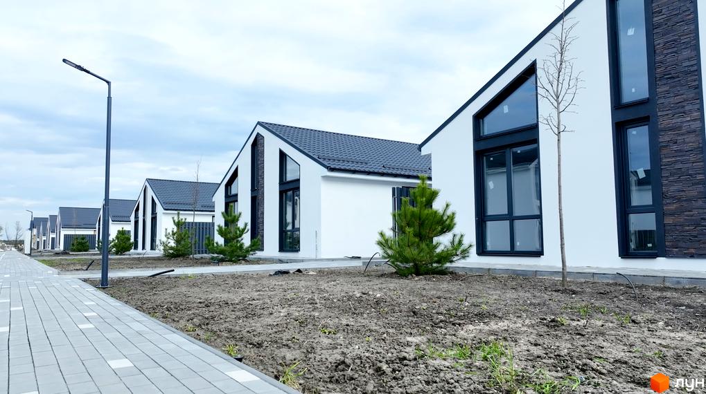 Котеджне містечко KМ Gardd House Eco Village: білі будинки з темними дахами та великими вікнами, вимощені доріжки та зелені насадження.