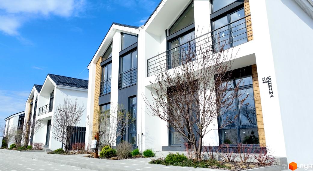 Котеджне містечко КМ Gardd House Eco Village: фасади будинків з великими вікнами та балконами, прибудинкова територія з деревами та кущами.