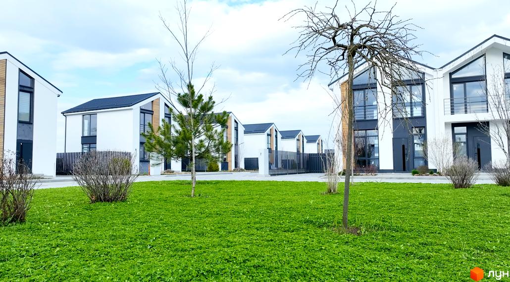 Котеджне містечко КМ Gardd House Eco Village. Білі двоповерхові будинки з темними дахами та великими вікнами, зелений газон та дерева.