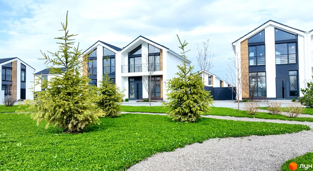 Котеджне містечко КМ Gardd House Eco Village. Зовнішній вигляд будинків з великими вікнами та прибудинкова територія з зеленим газоном та деревами.