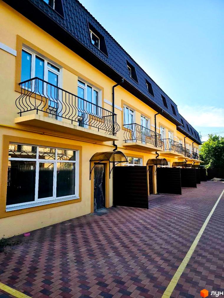 Зовнішній вигляд таунхаусів Родинний Преміум 2 з жовтим фасадом та чорним дахом, вимощена доріжка перед будинками.