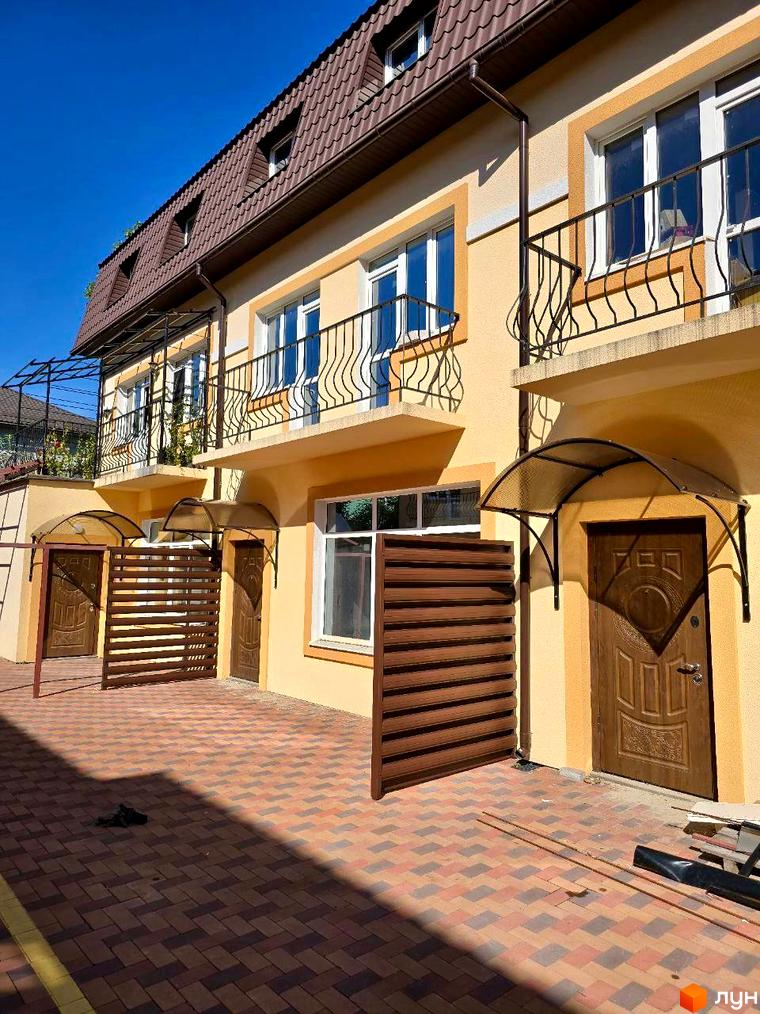 Зовнішній вигляд таунхаусів Родинний Преміум 2 з коричневим дахом та жовтими стінами, з бруківкою на прибудинковій території.