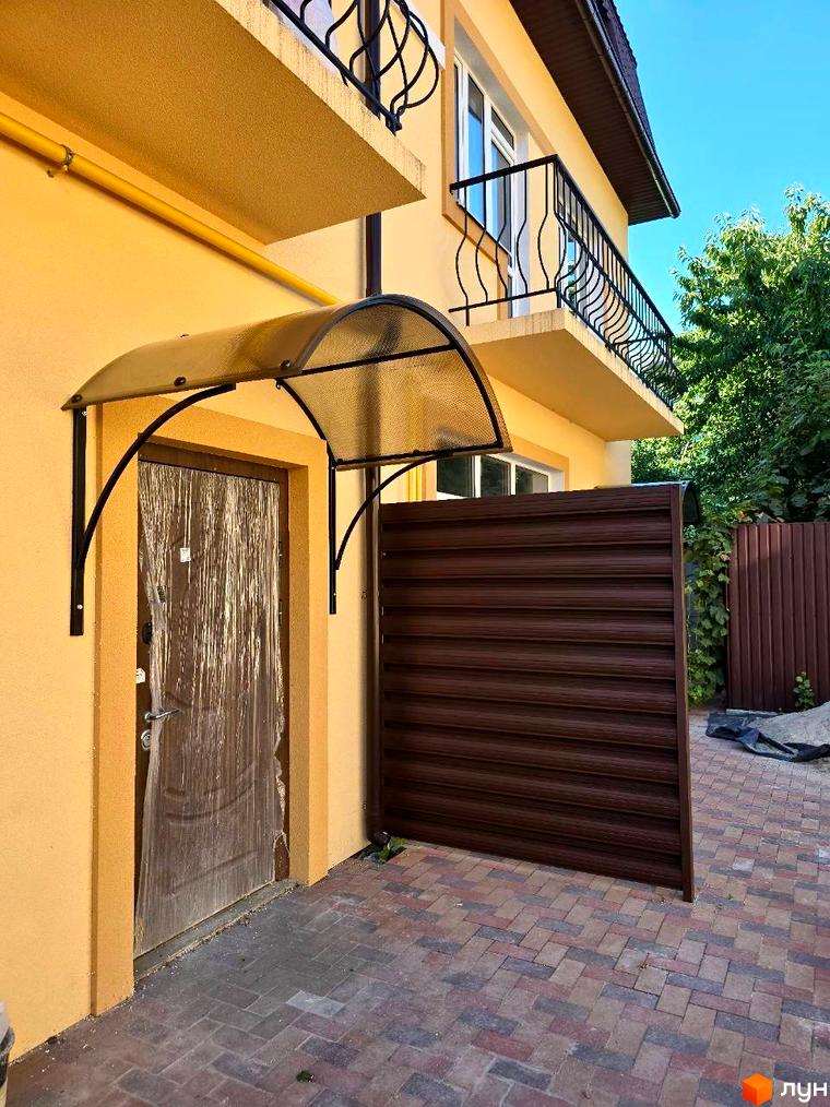 Зовнішній вигляд будинку Таунхауси Родинний Преміум 2 з жовтим фасадом, балконами та вхідною групою. Прибудинкова територія з коричневим парканом та бруківкою.