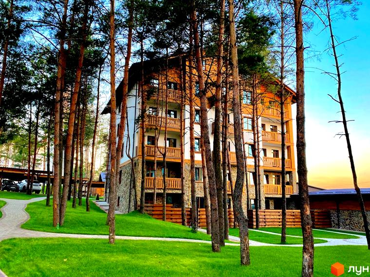 Житловий комплекс DESNA residence з дерев'яними балконами та кам'яним фасадом, оточений соснами та доглянутим газоном.