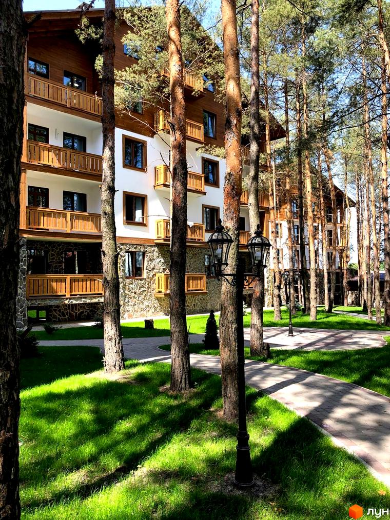 Житловий комплекс DESNA residence з дерев'яними елементами та балконами, оточений соснами та доглянутою зеленою територією з доріжками.