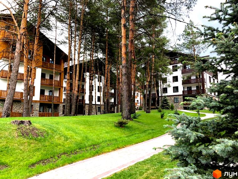 Житловий комплекс DESNA residence з дерев'яними елементами та балконами, оточений соснами та доглянутою зеленою територією з доріжками.