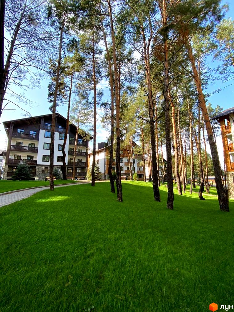 Житловий комплекс DESNA residence з білими фасадами та дерев'яними елементами, оточений високими соснами та доглянутим зеленим газоном.