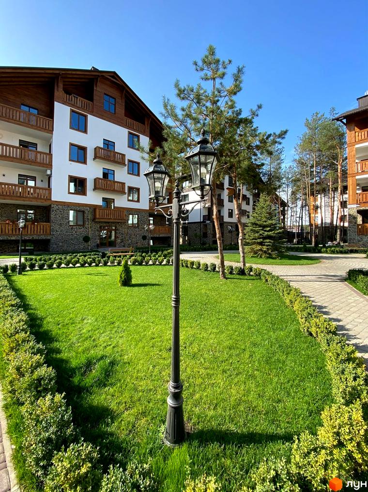 Житловий комплекс DESNA residence з білими фасадами, дерев'яними елементами та балконами, оточений зеленим газоном та доглянутими кущами.