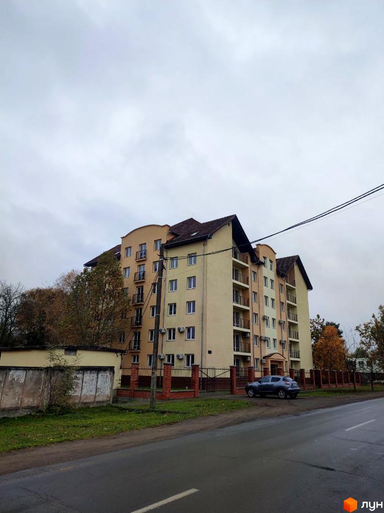 Житловий комплекс на вул. Хмельницького, 163/1 з бежевим фасадом, балконами та коричневим дахом. Перед будинком дорога, огорожа та припаркований автомобіль.