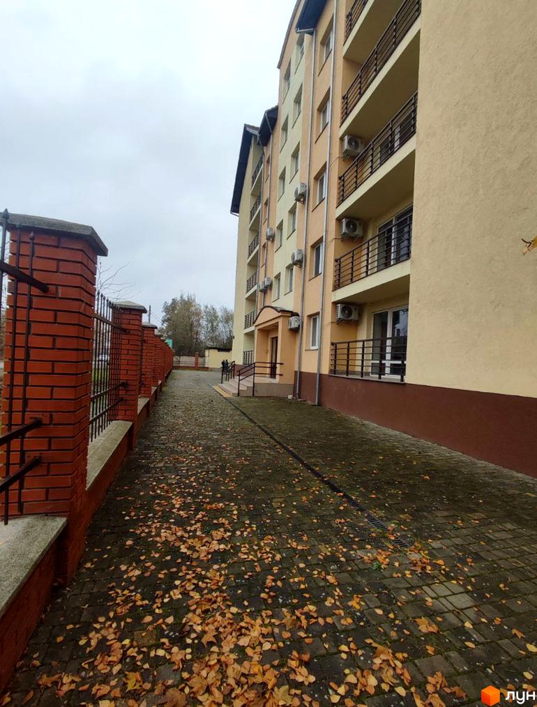 Зовнішній вигляд будинку по вул. Хмельницького, 163/1, з цегляною огорожею та бруківкою, покритою опалим листям.