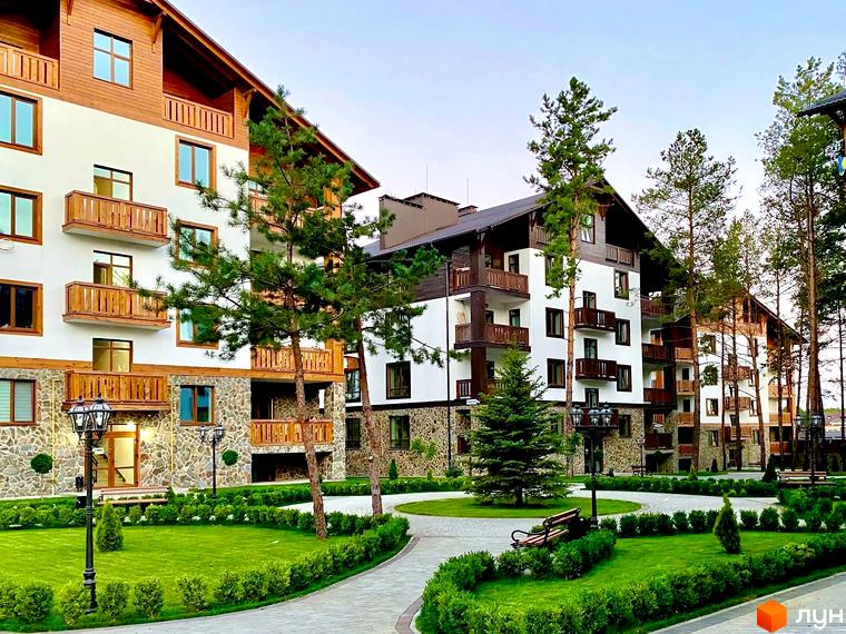 Житловий комплекс DESNA residence: багатоповерхові будинки з білими фасадами, дерев'яними балконами та кам'яним цоколем. Територія з доглянутими газонами, доріжками та соснами.